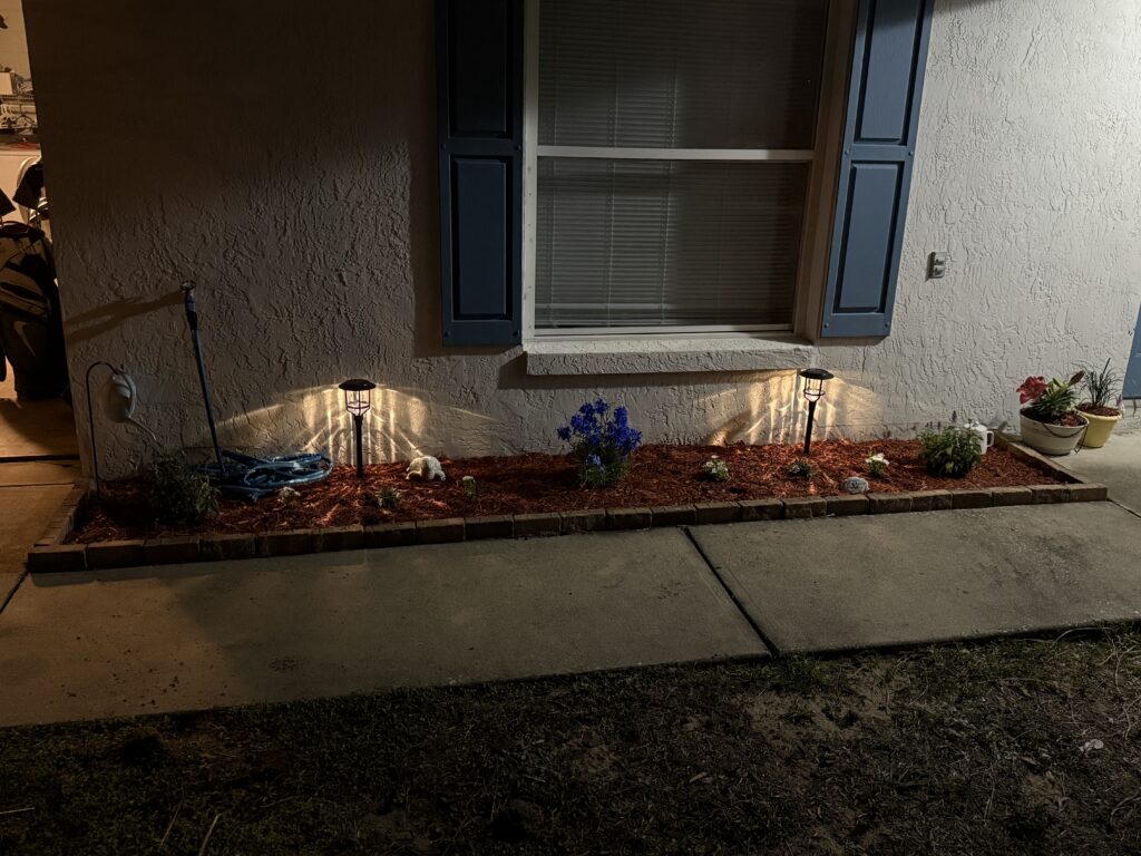 Completed red mulch installation with fresh plantings and solar path lights in Ocala FL foundation bed