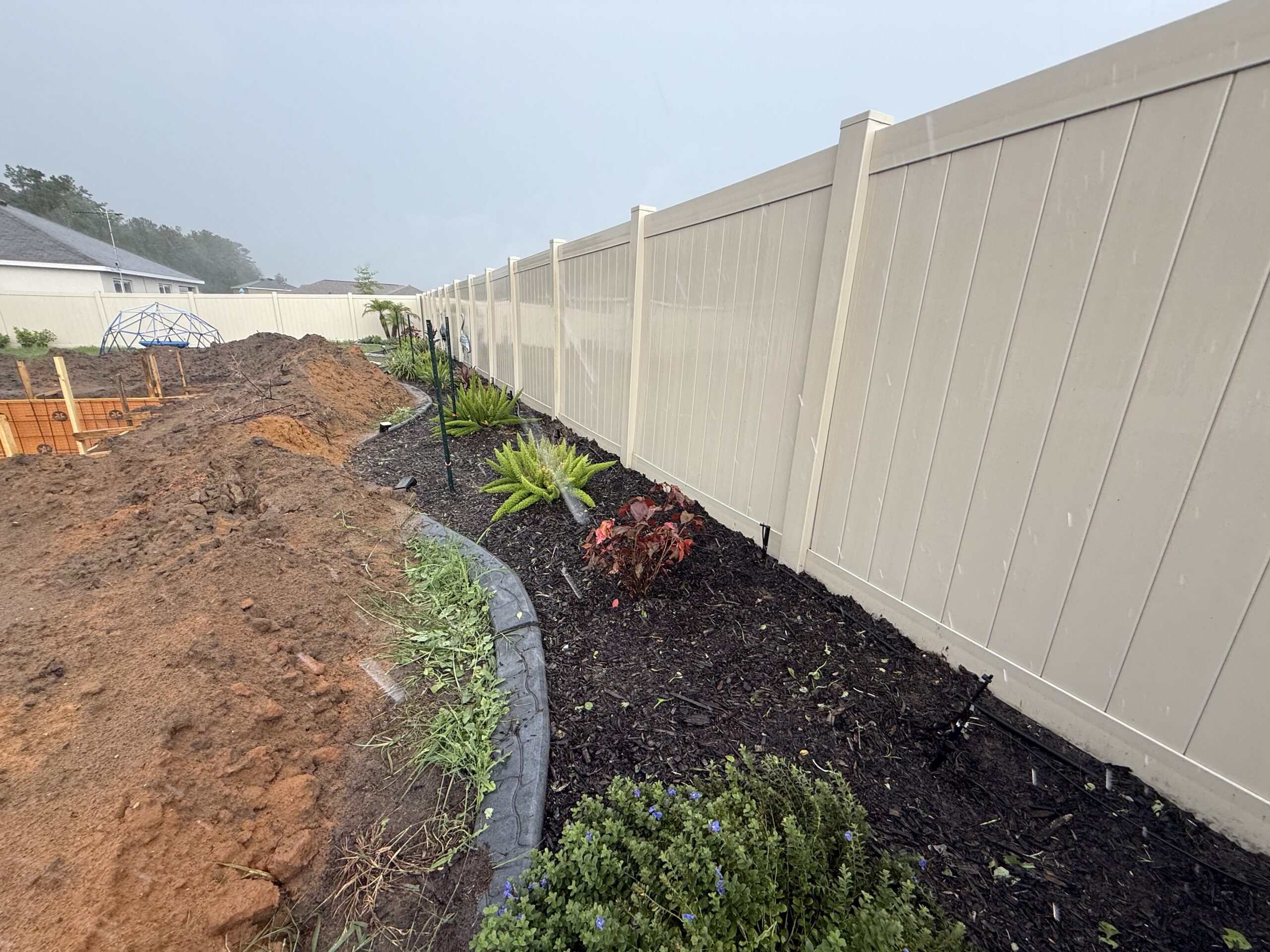 Fresh dark mulch bed with new small plantings along white vinyl fence in Ocala FL